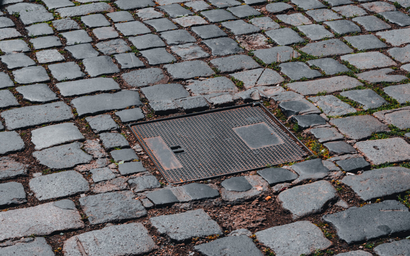 Square shape sewer cap or manhole cover n a paved road with cobblestone